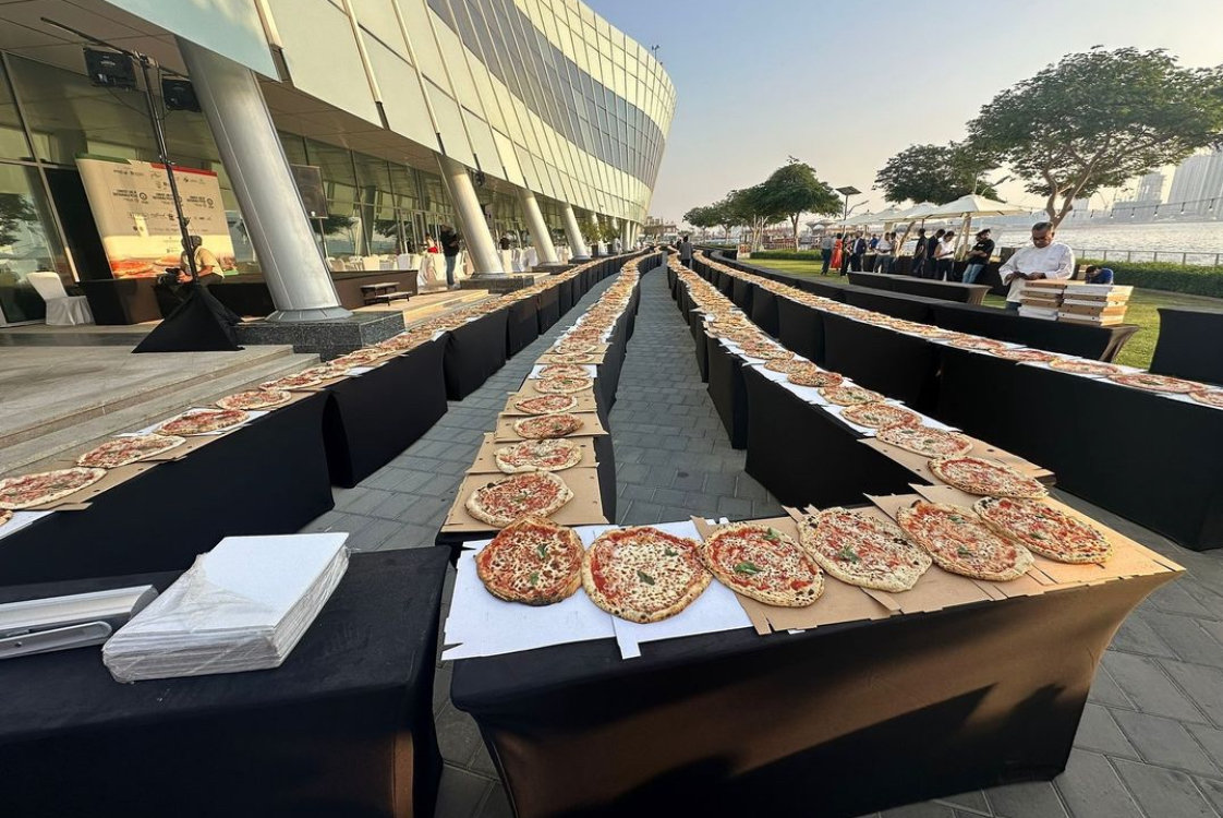This photo shows four rows of pizzas arranged in lines as far as you can see.