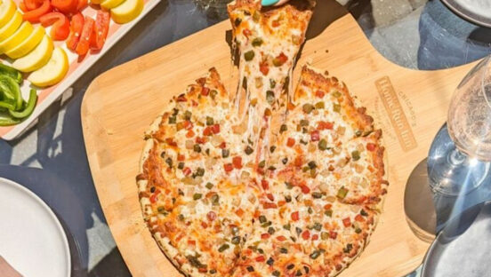 This photo shows a woman's hand, with fingernails painted a light blue, pulling a slice from a whole pie topped with sausage and peppers.