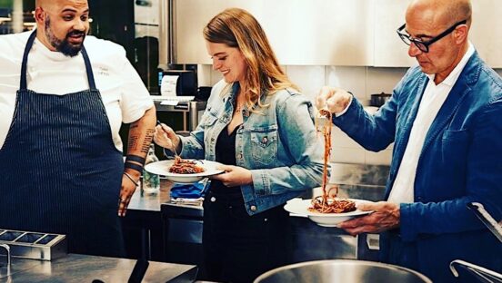 This photo shows Chef Celso Laforgia in his kitchen, with Stanley Tucci on the right and a woman in the middle, the latter two eating one of Laforgia's pasta dishes.