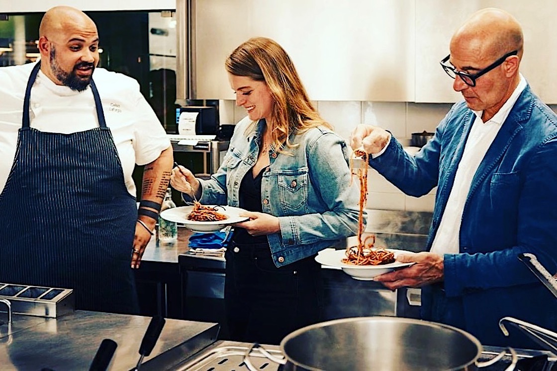 This photo shows Chef Celso Laforgia in his kitchen, with Stanley Tucci on the right and a woman in the middle, the latter two eating one of Laforgia's pasta dishes.