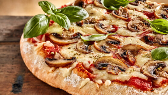This photo shows a pizza topped with mushrooms, tomatoes, cheese and basil.
