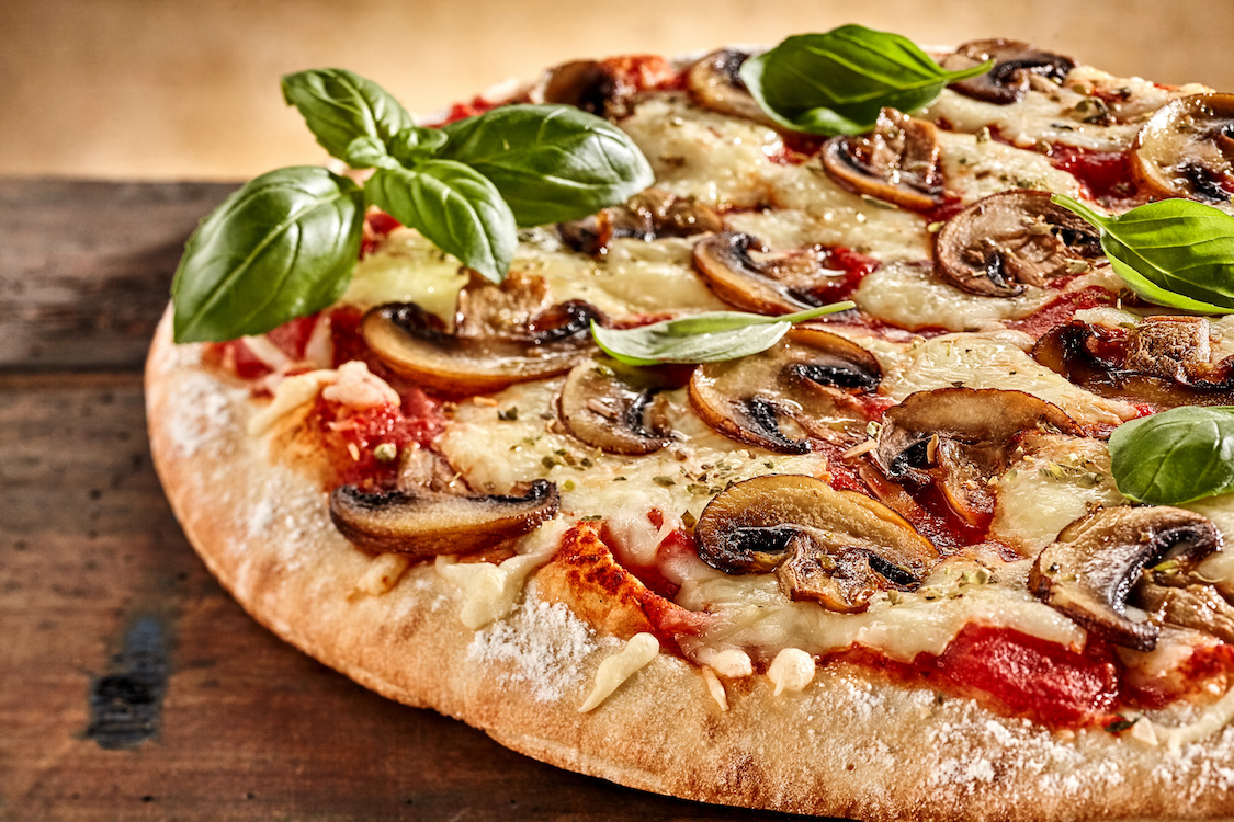 This photo shows a pizza topped with mushrooms, tomatoes, cheese and basil.