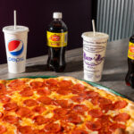 This photo shows a pepperoni pizza with cups of Pepsi and other soft drinks at Manco & Manco Pizza.