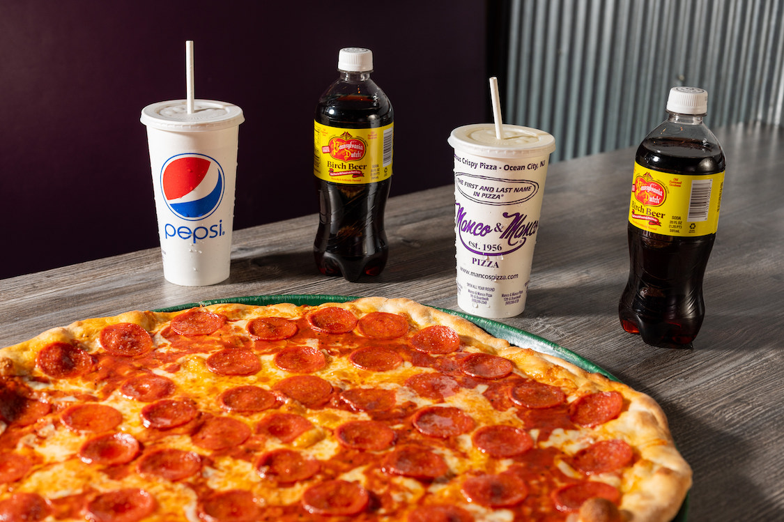 This photo shows a pepperoni pizza with cups of Pepsi and other soft drinks at Manco & Manco Pizza.