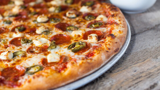 This photo shows a baked pizza with a raised edge topped with pepperoni, jalapeños and cream cheese.
