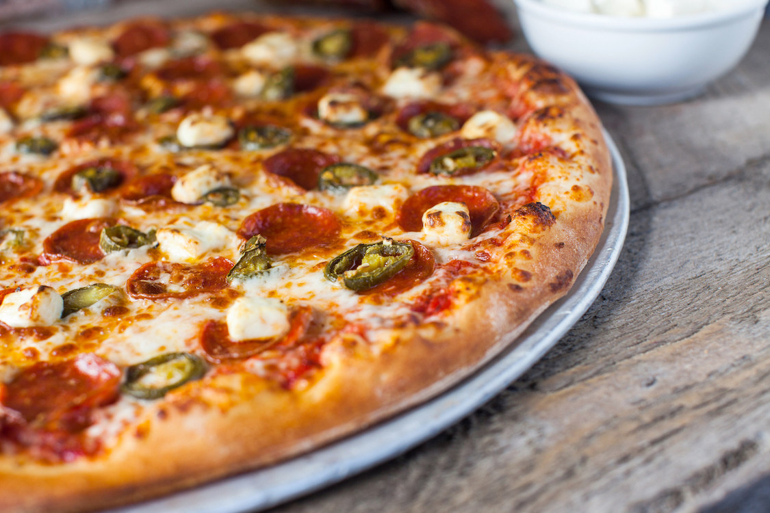 This photo shows a baked pizza with a raised edge topped with pepperoni, jalapeños and cream cheese.