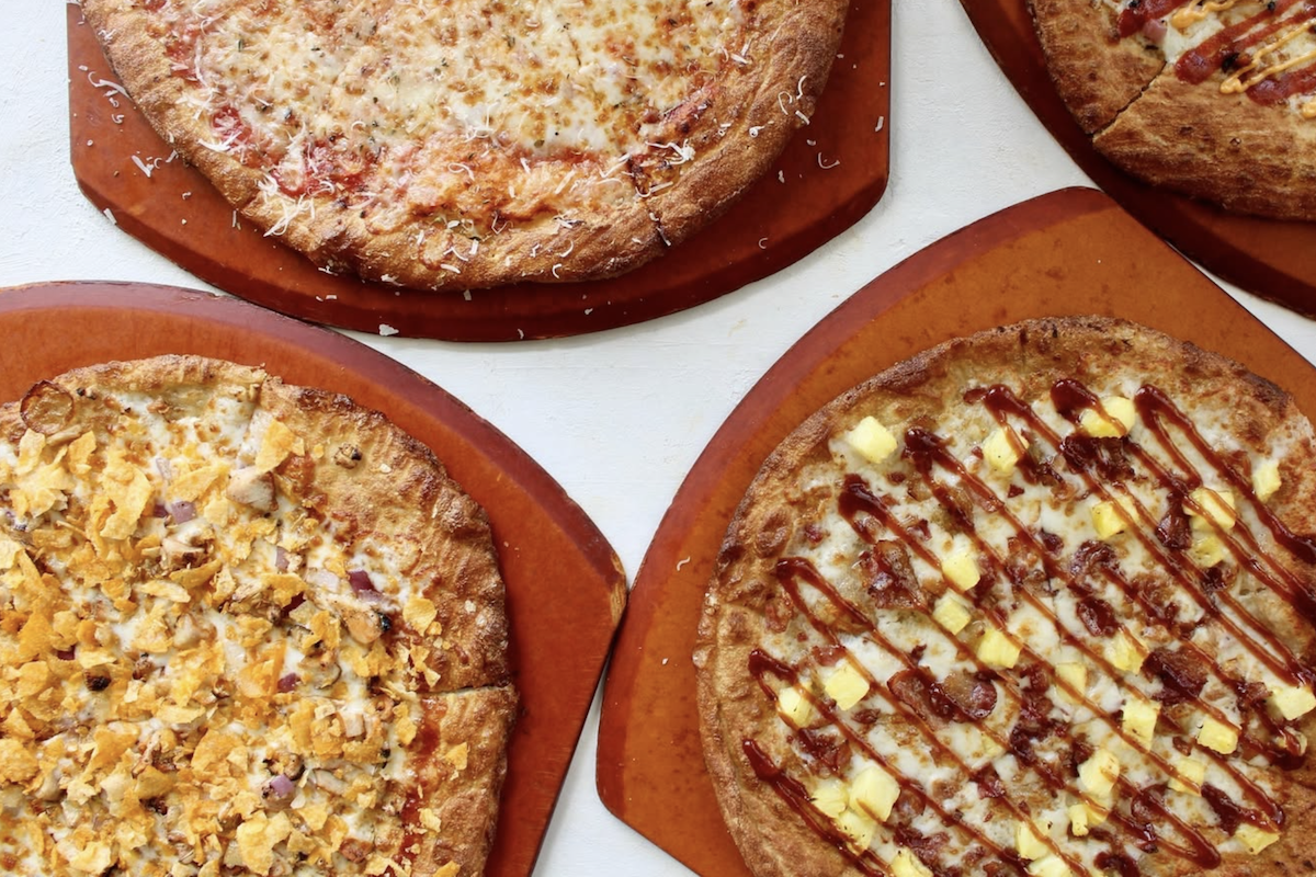 Four pizzas on peels with a white background.