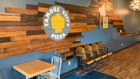 A shot of the interior of a pizzeria called Famous Yeti's. There are large slabs of wood on the walls and some chairs and tables set out.