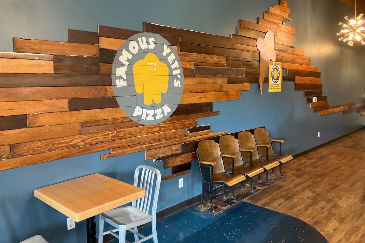 A shot of the interior of a pizzeria called Famous Yeti's. There are large slabs of wood on the walls and some chairs and tables set out.