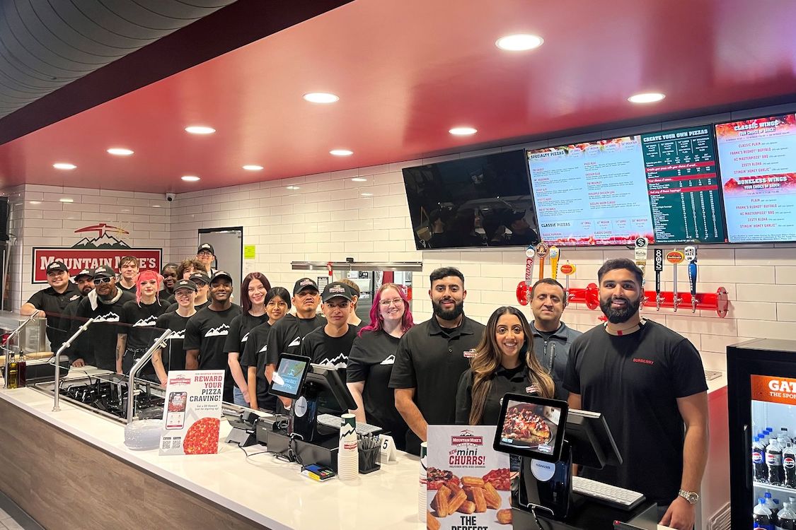 This photo shows a large group of employees assembled behind the counter at a Mountain Mike's restaurant.