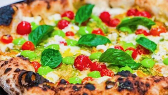This photo shows a pizza topped with basil leaves, cherry tomatoes and other colorful toppings.