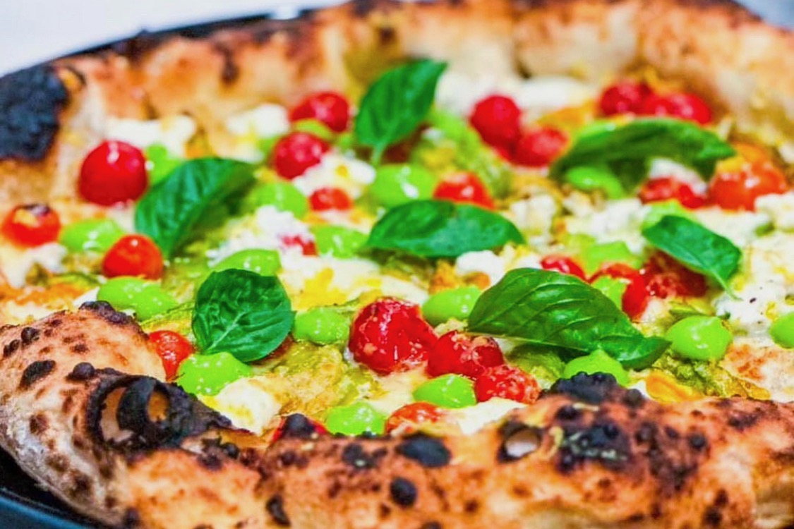 This photo shows a pizza topped with basil leaves, cherry tomatoes and other colorful toppings.
