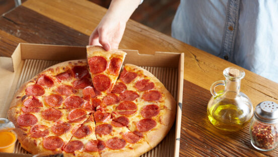 This photo shows a woman's hand pulling a slice of pepperoni pizza from a whole pie in a Romeo's Pizza delivery box.