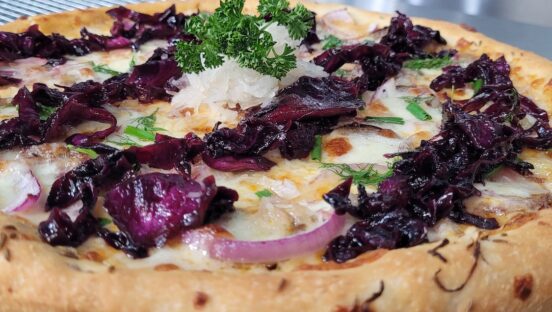 This photo shows a pizza topped with sauerkraut, sausage, red cabbage and a rahm sauce.