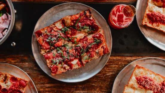 This photo shows a beautiful square-shaped Detroit-style pizza with cheese, sauce, tomato slices and strips of basil.