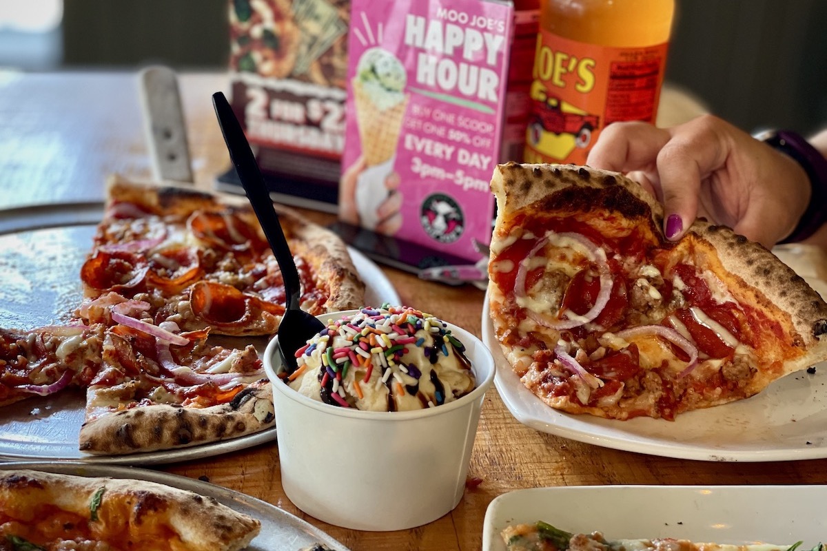 A full array of pizza and ice cream on a table inside of a restaurant.