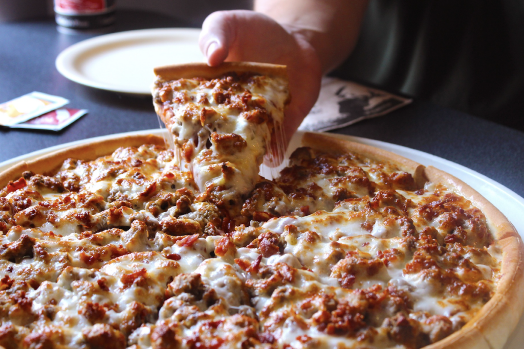A hand pulls a slice of bacon lover's pizza from Godfather's Pizza.