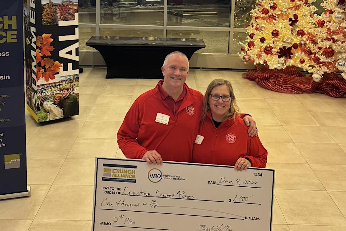 This photo shows the husband-and-wife owners, both dressed in red, with an oversized check for $1,000 at the Titletown Tech event. for entrepreneurs.
