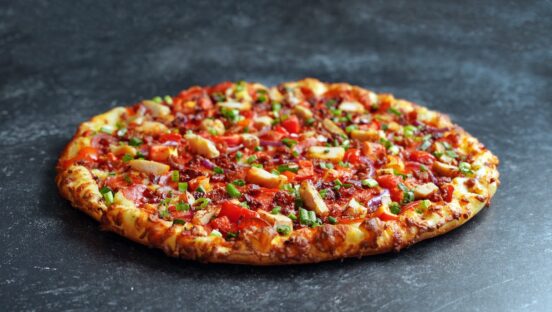 A large pizza with several toppings, including chicken, bacon and pepperoni.
