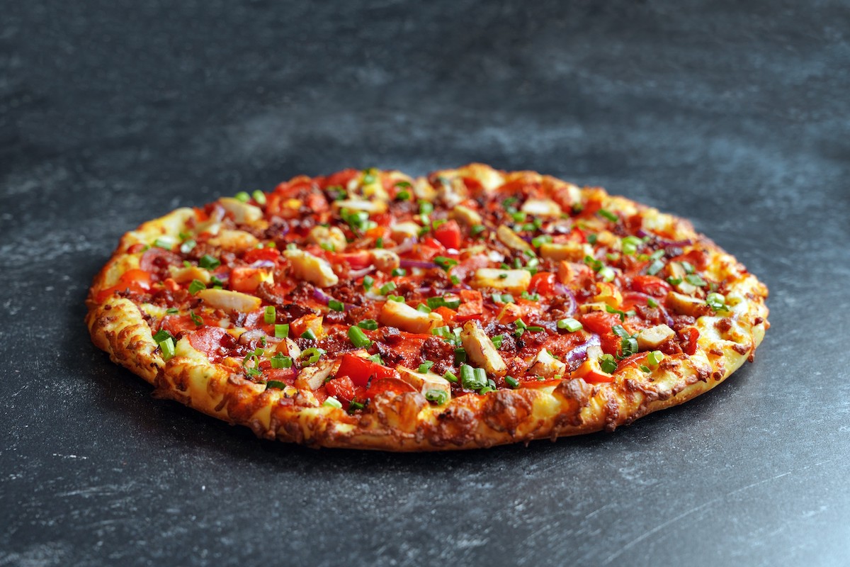 A large pizza with several toppings, including chicken, bacon and pepperoni.