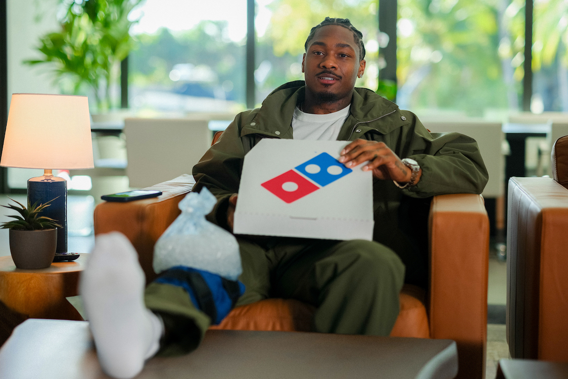 This photo shows NFL player Stefon Diggs relaxing in his living room with a Domino's pizza box, one foot propped up on a leg rest in front of him.