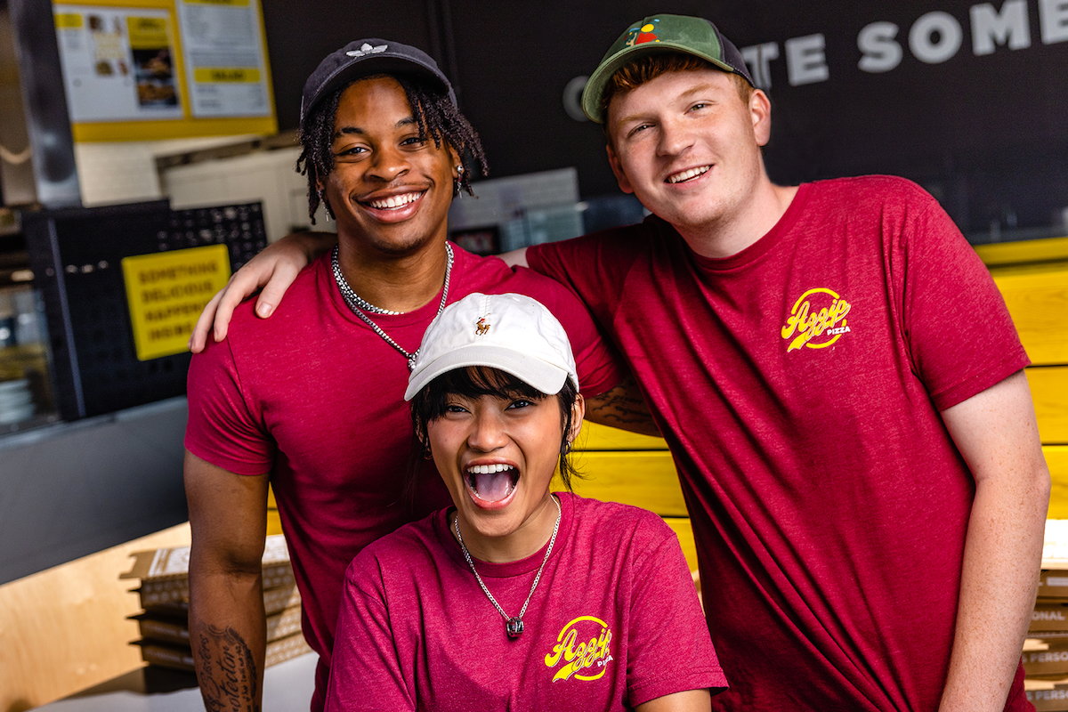 Three Azzip Pizza team members smile into the camera.