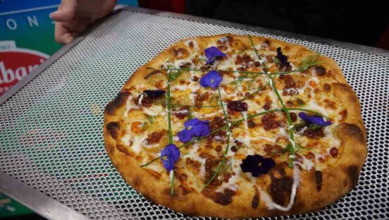 This photo shows a pizza topped with pretty blue flowers and other ingredients.