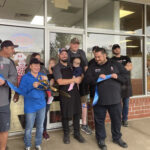This photo shows Michael LaMarca, wearing a black chef coat, right after he and a team member cut the ribbon at the grand opening of a Master Pizza location. Standing nearby are several other employees, most wearing black shirts, and one of them is holding a baby.