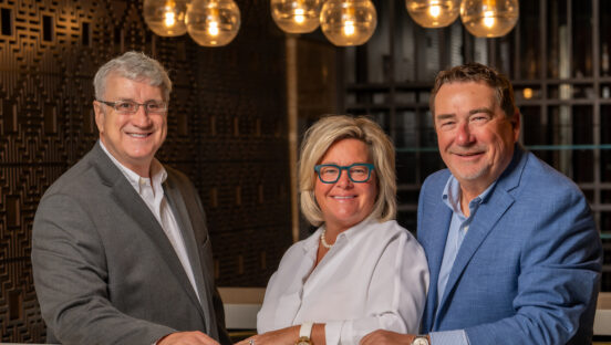 Three people stand posing in a restaurant, looking directly into the camera.