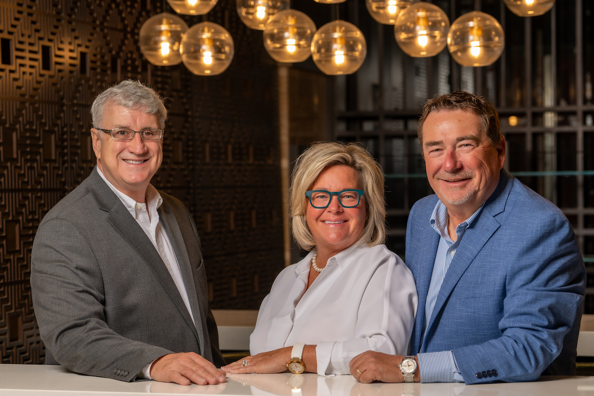 Three people stand posing in a restaurant, looking directly into the camera.