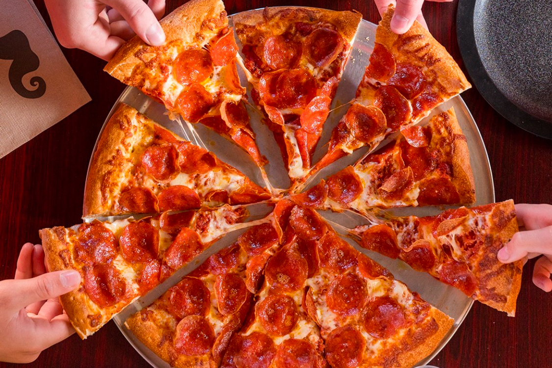 This photo shows a group of people's hands pulling slices out of a whole pepperoni pizza.