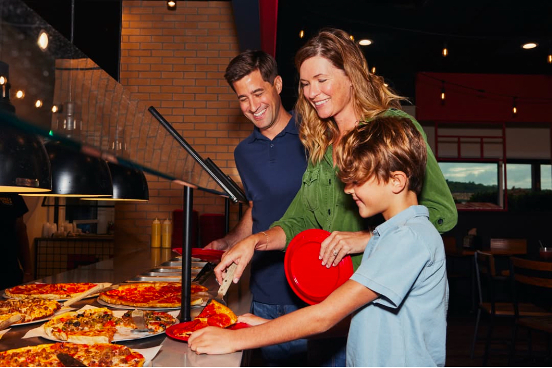 This photo shows a man, woman and young boy getting ready to load their plates at a Pizza Inn buffet bar.