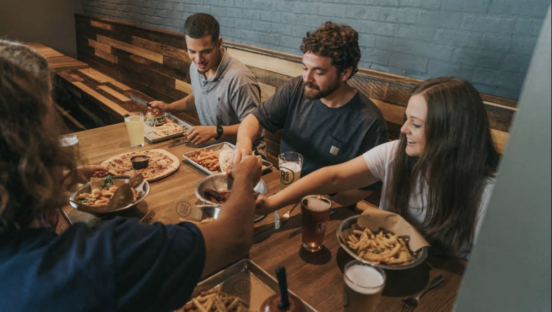 People gathered around a table reach for pizza in the middle.