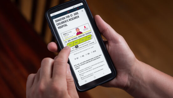 This photo shows a person's hands holding a smartphone with Domino's ordering screen, inviting customers to donate to St. Jude Children's Research Hospital.