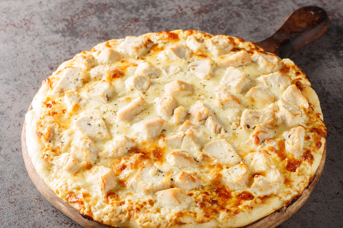 This photo shows a pizza with a white sauce topped with chicken.