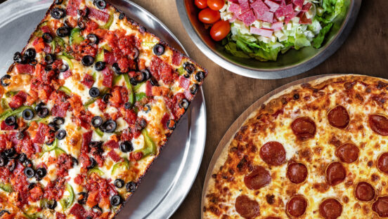 This photo shows two delicious-looking round Detroit-style pizzas and a salad from Buddy's Pizza.