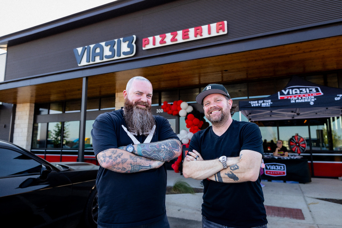 This photo shows Brandon and Zane Hunt in front of a Via 313 store, smiling, wearing black T-shirts, with their tattooed arms crossed.