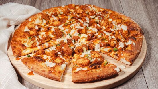 This photo shows a pizza topped with fried Nashville hot chicken, pickles and green onions, plus a drizzle of ranch.