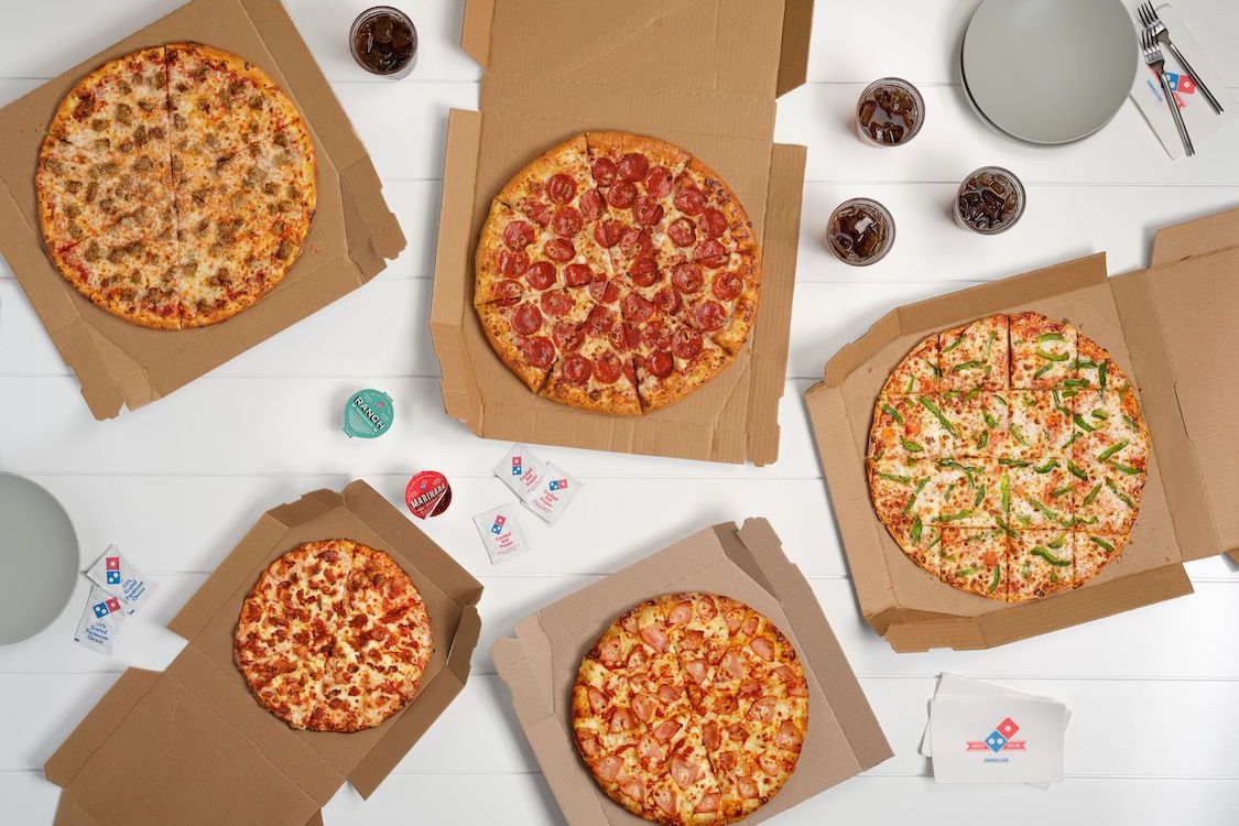 This photo shows a wide selection of Domino's pizzas in cardboard boxes.