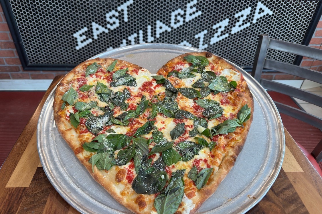 This photo shows a heart-shaped Margherita pizza loaded with whole basil leaves.