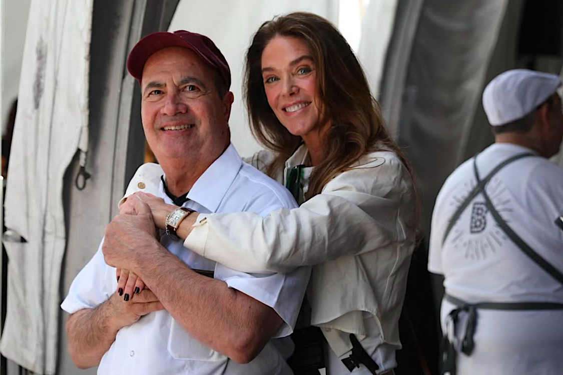 This photo shows John Arena in a white chef coat, and behind him Donna Baldwin is hugging him affectionately.