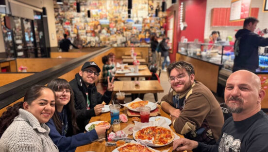 This photo shows a group of four people sitting at a table in a MOD restaurant with pizzas in front of them. They're all looking at the camera and smiling.
