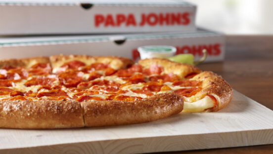 This photo shows a side view of a pepperoni pizza placed in front of two Papa Johns delivery boxes.