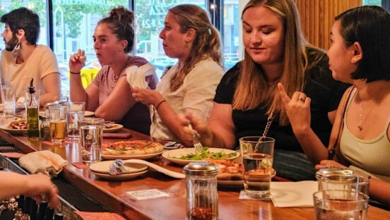 This photo shows a group of female customers eating pizza and other items at the bar at Pizzeria Paradiso.