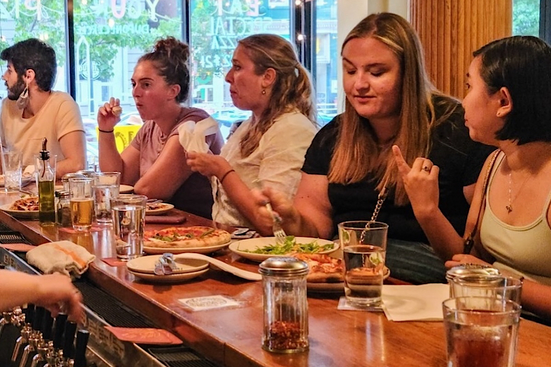 This photo shows a group of female customers eating pizza and other items at the bar at Pizzeria Paradiso.