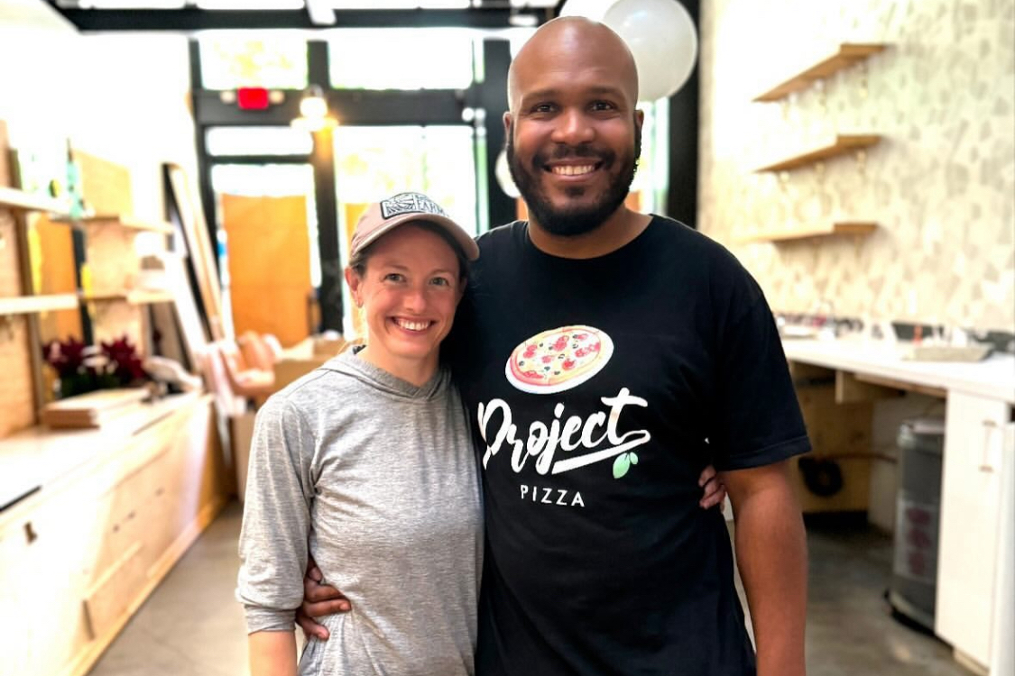 This photo shows the married couple, smiling and with their arms around each other, who own Pizza by Ruffin.