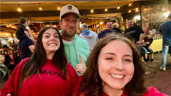 This photo shows Dave Portnoy with two young women dressed in red at The NONA Slice House.