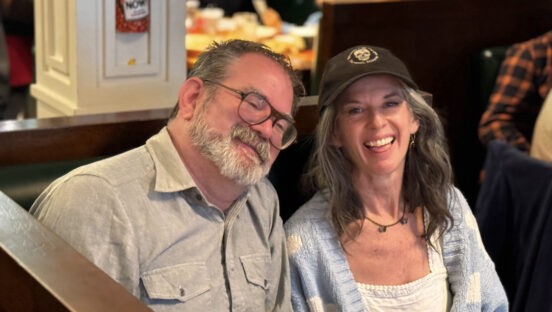 This photo shows Andrea, wearing a cap, sitting in a booth next to her bearded twin brother.