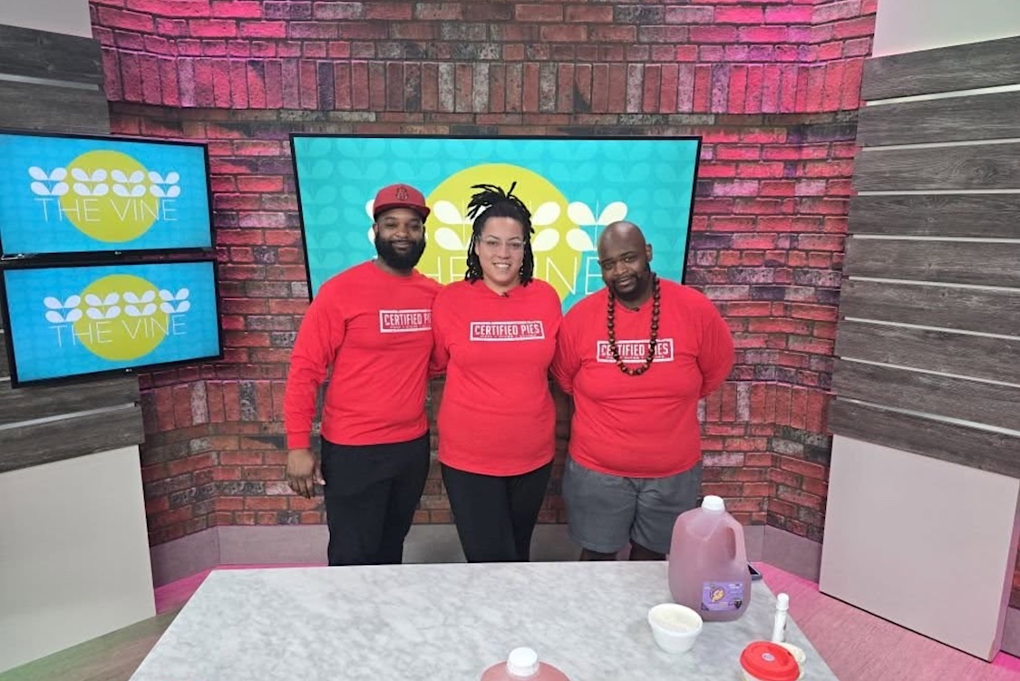 This photo shows the three owners of Certified Pies, all wearing red shirts branded with their logo, standing in a TV station side by side.