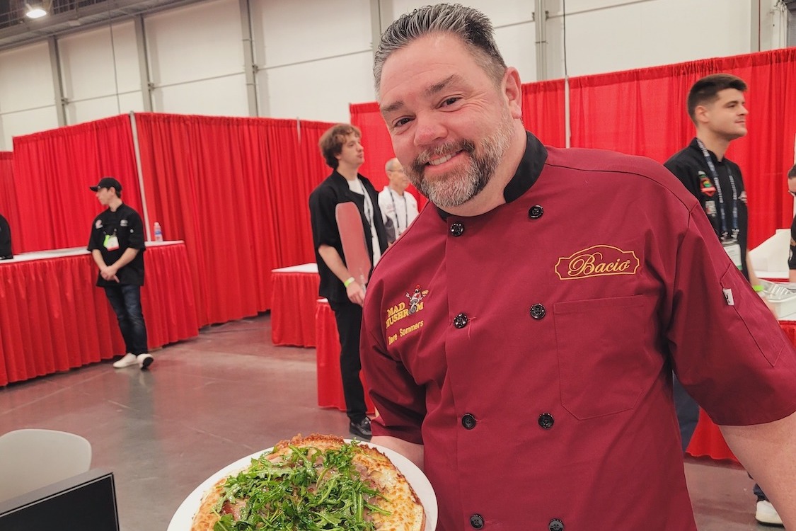 This photo shows Dave Sommers in a red chef coat holding a pizza.